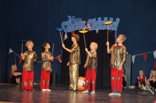 Vier kinderen met ronddraaiende bordjes op stokjes, op achtergrond logo Circus Okidoki